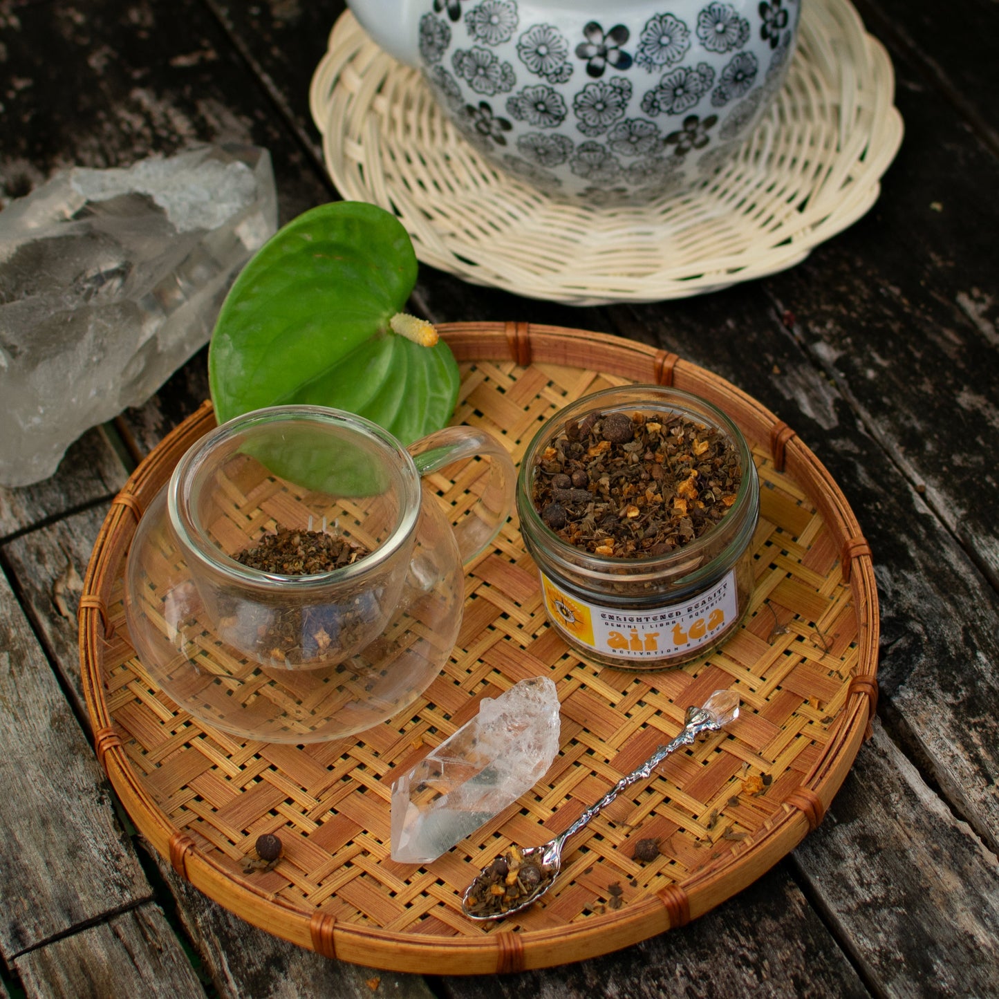 Glass teacup with loose herbal tea, crystal, and teapot on wooden table – Air Tea blend for activation rituals