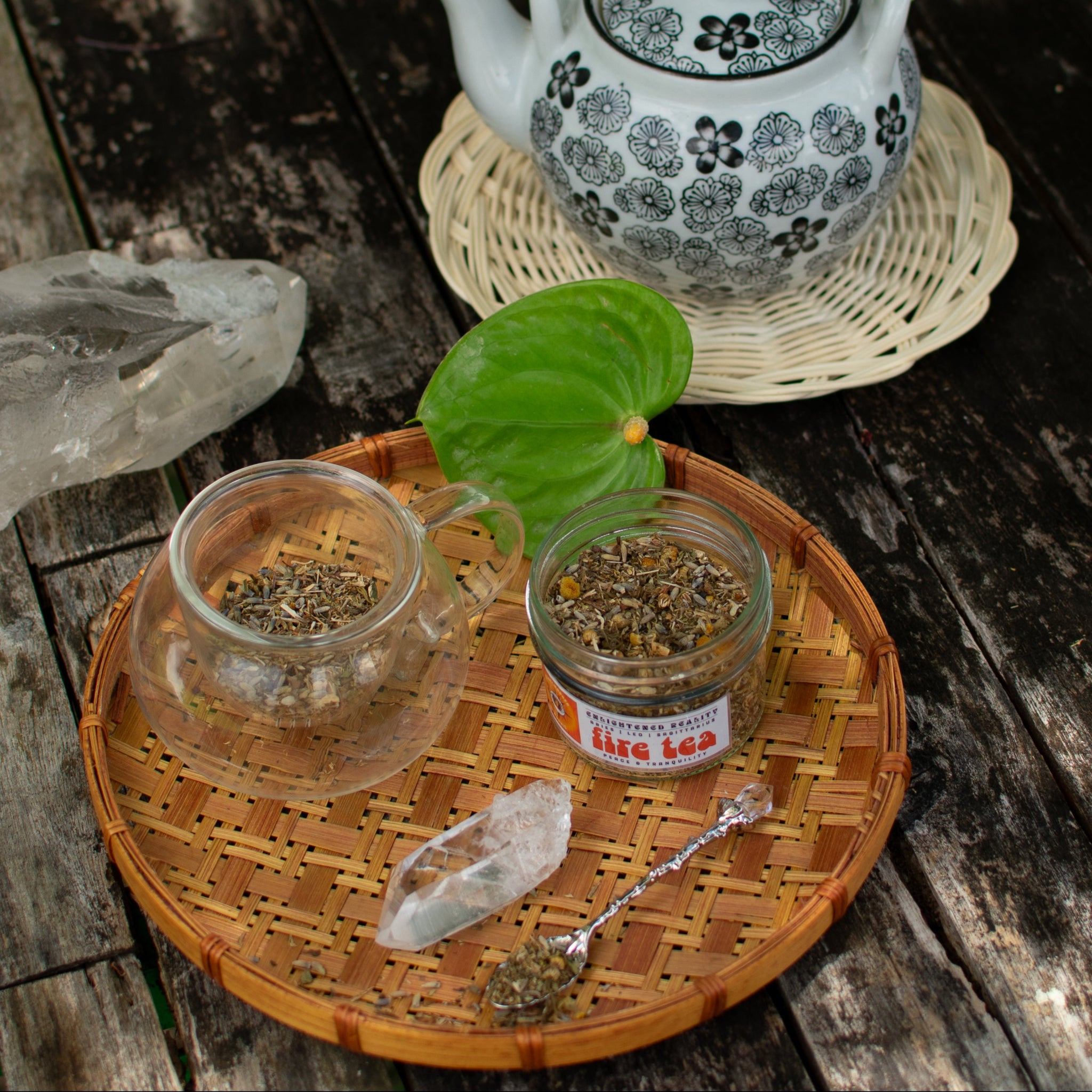 Glass teacup with loose herbal tea, crystal, and teapot on wooden table – Fire Tea blend for grounding rituals