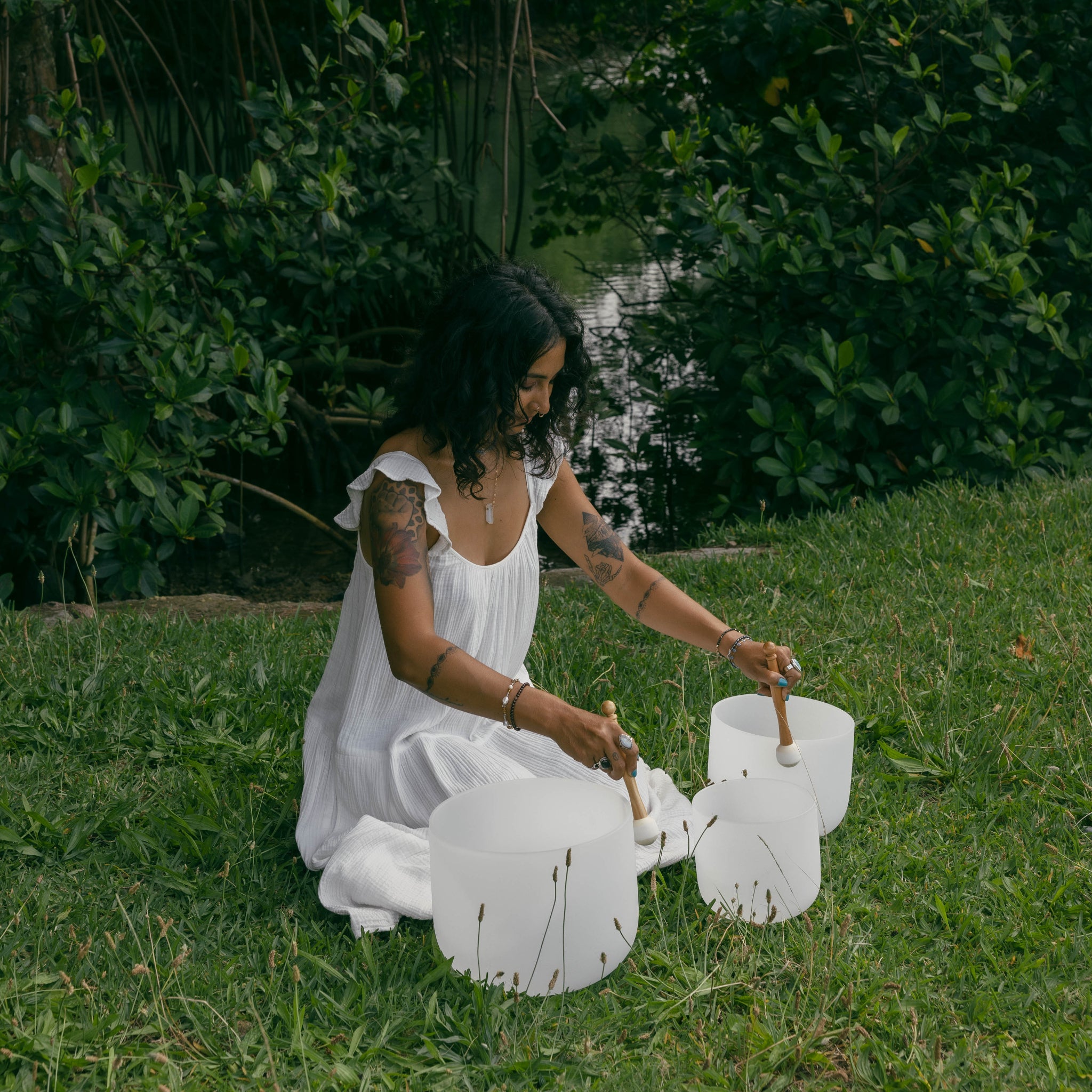 Woman in a white dress playing a set of white singing bowls outdoors.