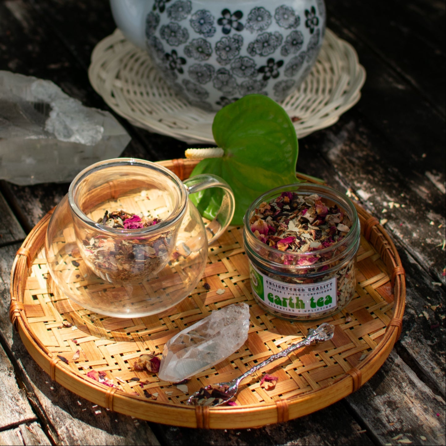 Glass teacup with loose herbal tea, crystal, and teapot on wooden table – Earth Tea blend for grounding rituals