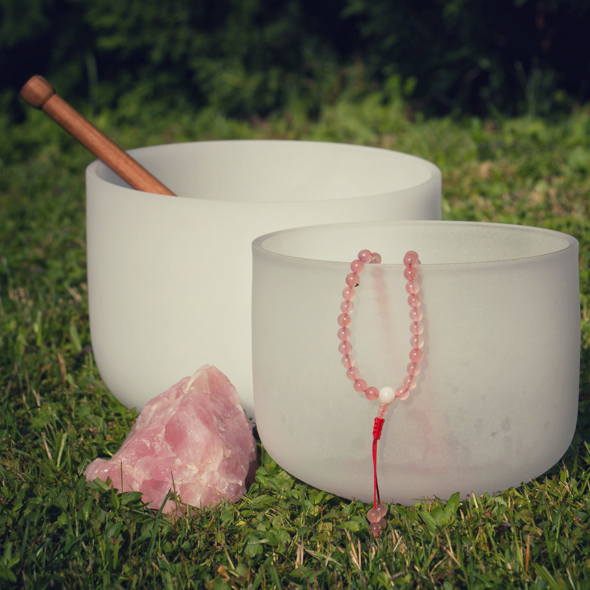crystal singing bowls are displayed next to rose quarts and spiritual natural stone beads for a sound bath service